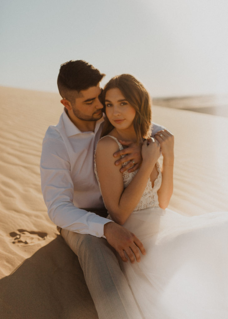 couple sitting together in the sand, with arms around each other